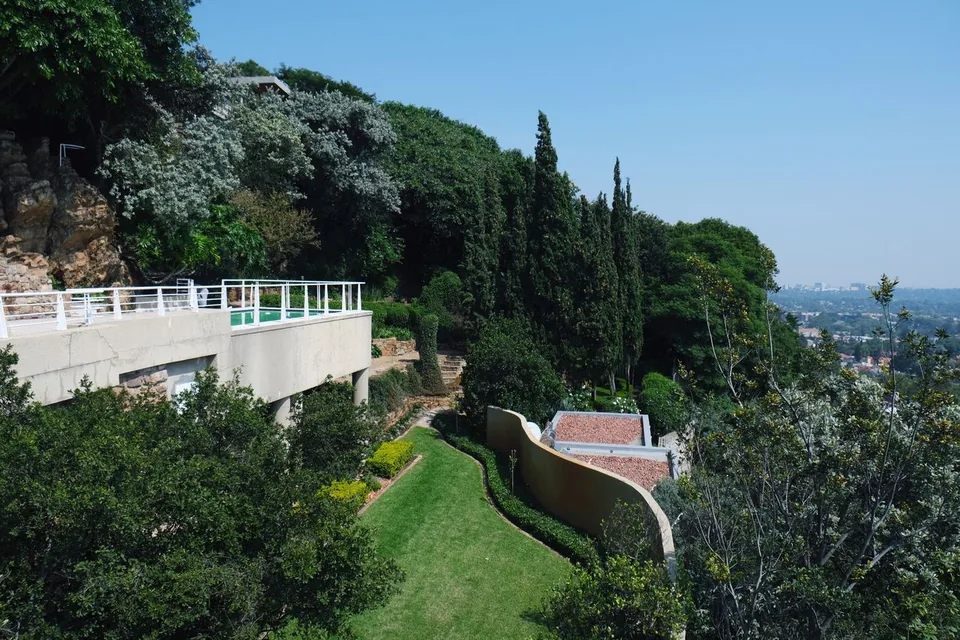 Elevated daytime view across the pool deck, curved event lawn, garden terraces and Johannesburg